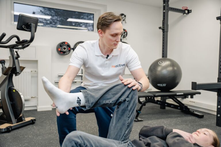 Fizjoterapeuta w Reactive stabilizuje kolano pacjentki podczas treningu medycznego, dbając o poprawny wzorzec ruchu po kontuzji.