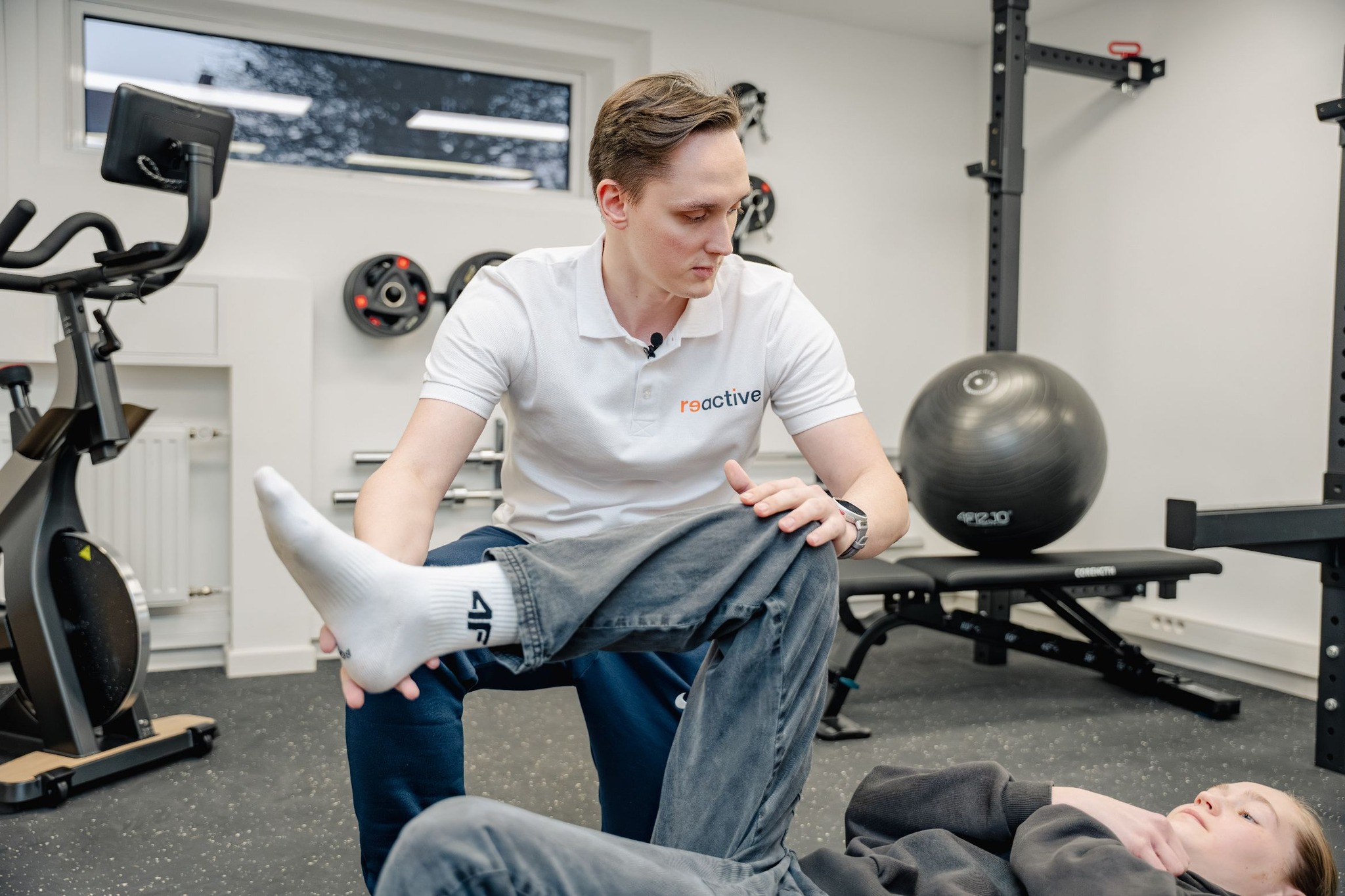 Fizjoterapeuta w Reactive stabilizuje kolano pacjentki podczas treningu medycznego, dbając o poprawny wzorzec ruchu po kontuzji.