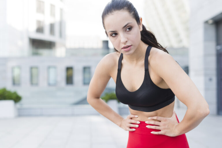 Biegaczka w stroju sportowym w plenerze trzymająca się za podbrzusze. Dyskomfort i wysiłkowe nietrzymanie moczu u sportowców to częsty problem, który leczy fizjoterapia uroginekologiczna w Reactive Warszawa Ursus.