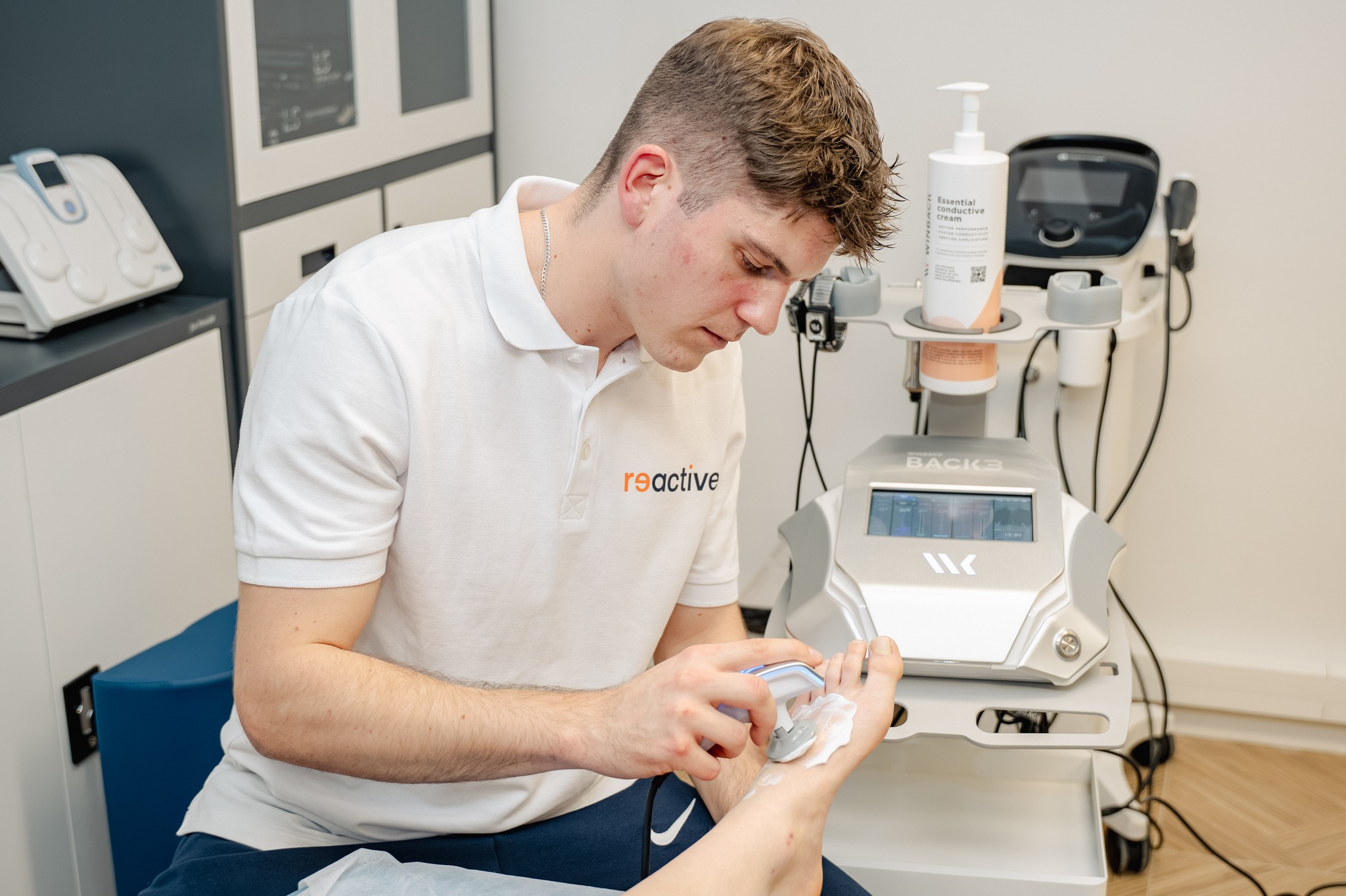 Fizjoterapeuta sportowy z kliniki Reactive Warszawa Ursus wykonuje zabieg innowacyjnej terapii Tecar na stopie pacjenta, używając specjalnej głowicy do głębokiego przegrzewania tkanek.